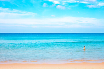 Blue sea with a strip of sandy beach and blue sky. In the background, a child enters the water. Seascape on a sunny day in the tropics