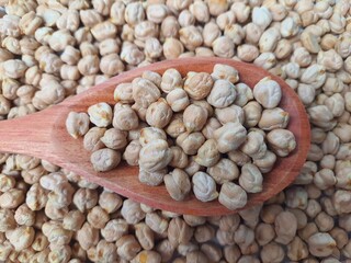 Chickpeas (Cicer arietinum) in a wooden spoon, chickpeas background, selective focus. It is also known by the names: Gravanço, Herbanzo, Chicken Pea or Bengal Pea or Duck Grain.
