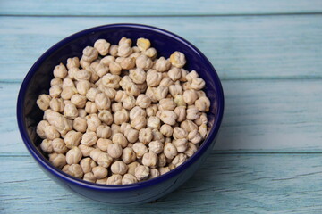 Chickpeas (Cicer arietinum), in a blue crockery bowl, isolated on wooden table, top view. It is also known by the names: Gravanço, Herbanzo, Chicken Pea or Bengal Pea or Duck Grain.
