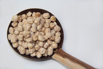 Chickpeas (Cicer arietinum), in a wooden spoon made with coconut shell, isolated on a wooden table. It is also known by the names: Gravanço, Herbanzo, Chicken Pea or Bengal Pea or Duck Grain.