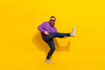 Full length photo of handsome positive guy dressed purple sweater eyewear dancing playing leg guitar isolated yellow color background