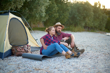 Fototapeta na wymiar relaxing couple of woman and man sit near tent in camping, hugs, spend time together in weekend