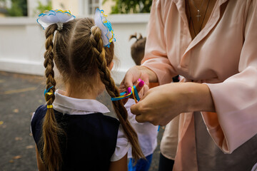 Shallow depth of field (selective focus) details with the hands of a teacher making a Ukrainian flag bow in the hair of a girl pupil.