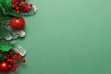 Bright Christmas border made with fir tree branches, berries and bright balls on green background...