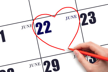 A woman's hand drawing a red heart shape on the calendar date of 22 June. Heart as a symbol of love.