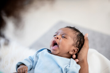 1 month old African American baby newborn is yawning sleepy while lying on the palm of his mother, to family and infant newborn concept. - obrazy, fototapety, plakaty
