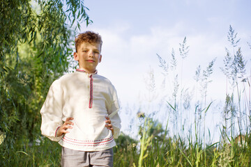 Portrait of a little boy in a white traditional embroidered shirt against the sky in the garden in summer. Freedom, national costume, childhood