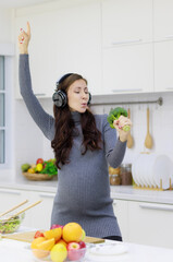 Beautiful, cool, pregnant woman happily cooking organic and healthy salads in her modern kitchen....