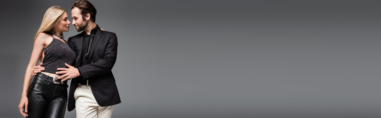 Side view of man in jacket hugging sexy blonde girlfriend isolated on grey, banner.