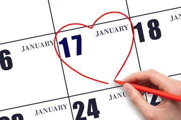 A woman's hand drawing a red heart shape on the calendar date of 17 January. Heart as a symbol of...