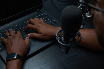 A black male blogger blogger posts content in his studio. Close up of the hand while typing at the...
