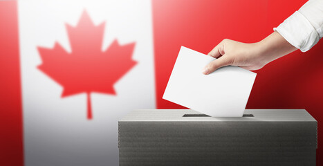Close-up hand holding ballot paper into the voting box an Canada flag background. Freedom democracy...