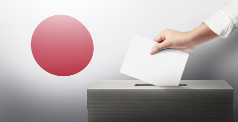 Close-up hand holding ballot paper into the voting box an Japan flag background. Freedom democracy concept. Freedom vote concept.