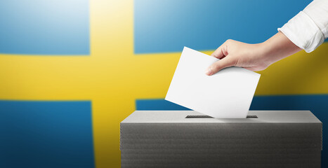 Close-up hand holding ballot paper into the voting box an Sweden flag background. Freedom democracy...