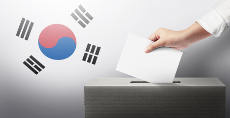 Close-up hand holding ballot paper into the voting box an South Korea flag background. Freedom democracy concept. Freedom vote concept.