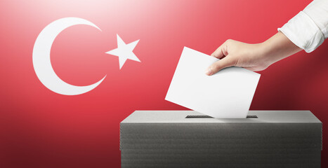 Close-up hand holding ballot paper into the voting box an Turkey flag background. Freedom democracy...