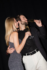 Positive woman in dress hugging boyfriend drinking champagne isolated on black.