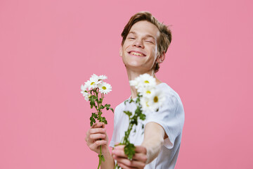 cute guy stretches a bouquet of white daisies into the camera