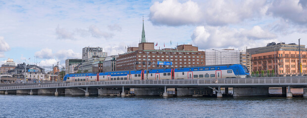 Blue commuting train Mälartåg passing a bridge down town a sunny day in Stockholm