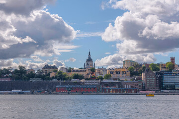 Obraz premium View over the district Södermalm with church, towers and harbor a sunny day with cumulus clouds in Stockholm