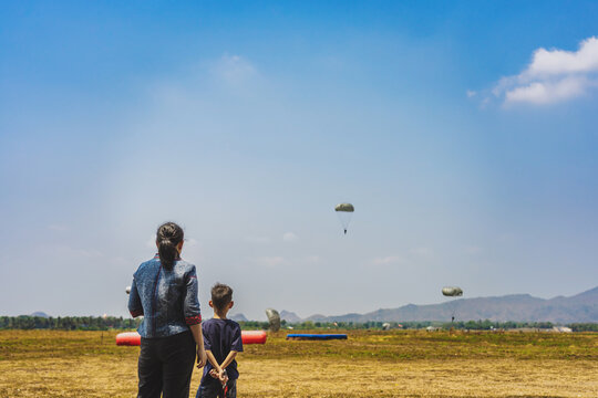 Back view of mother and son look with worry and concern during parachute training from airplane for army cadet with blurred image of parachute and landscape in background. Family relationship concept.