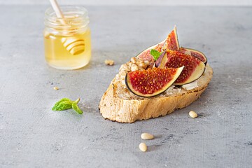 Crispy bruschetta (toast) with soft ricotta, ripe figs, walnuts and pine nuts, mint and honey on a light background.