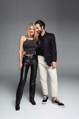 Smiling man hugging stylish girlfriend on grey background.