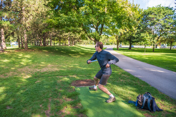 Disc golf, a flying disc sport played using rules like golf, being played by a middle aged man on a...