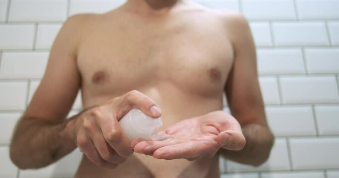 Unrecognizable man in the bathroom, sprays intimate gel lubricant on his fingers, drops fall down. Preparing for sex. Front view, close-up.