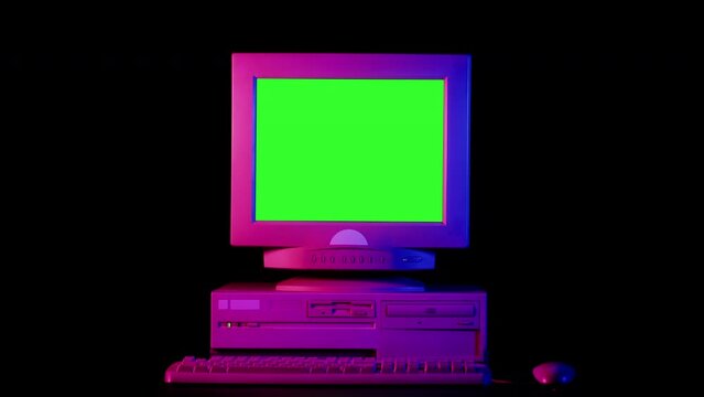 Old computer with green chroma key screen close-up, Desktop PC isolated on black background, neon pink illumination. Retro obsolete technology. 