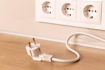 Power cord cable unplugged with group of white european electrical outlets on modern beige wall