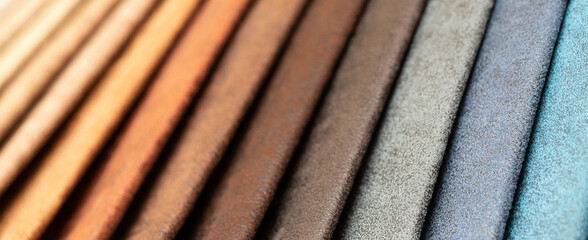 Fabric swatches in different colors are stacked for selection. A variety of shades of upholstery material for furniture and interior. Fabric texture close up. A set of multi-colored rolls of material.