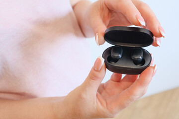 Woman with wireless headphones. Close up of woman is holding the black wireless earbuds case in hand