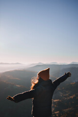 Happy woman from behind raises her hands up in front of the high mountains