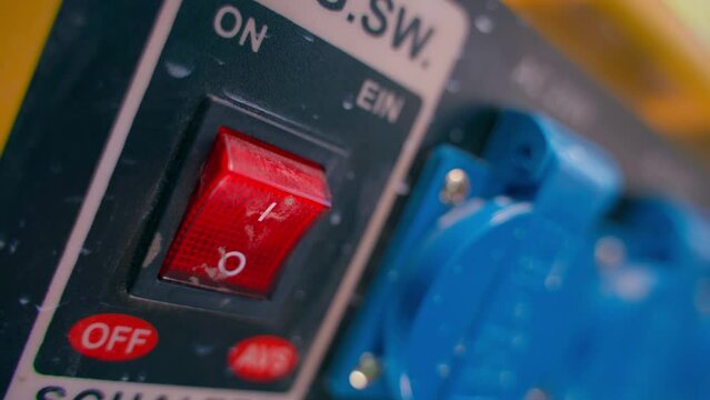 The finger presses the red off button on the gas generator housing against the background of blue power sockets. Shutdown of autonomous power supply