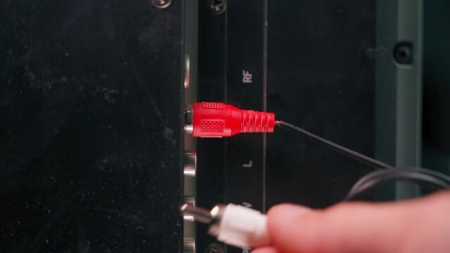 Hand inserts rca connectors of red white and yellow color from tv. Plug tulip of the old generation close-up. Wires for transmitting audio and video signals are thin, poor quality