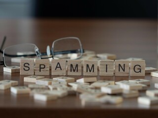 spamming word or concept represented by wooden letter tiles on a wooden table with glasses and a book - obrazy, fototapety, plakaty