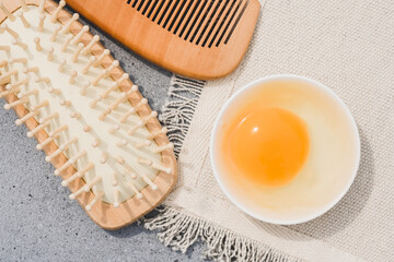 Raw egg in white bowl and wooden comb at concrete table. Making homemade hair mask with egg. Natural hair beauty treatment, zero waste handmade cosmetics