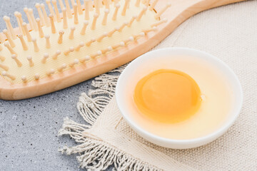 Raw egg in white bowl and wooden comb at concrete table. Natural hair beauty treatment. Zero waste...