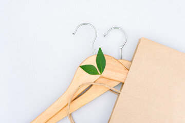 Green shopping concept. Wooden hangers, paper bag and green leaves over light gray background. Symbol of slow fashion. Reuse, recycling and upcycling clothes - obrazy, fototapety, plakaty