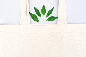 Green shopping concept. White cotton bag with green leaves over light gray background with copy space. Environmentally friendly shopping and sustainable lifestyle. Mockup image