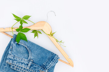 Upcycling clothes or creative reuse concept. Jeans on wooden hanger with green leaves over light...