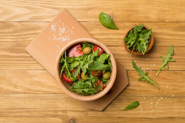 Fresh salad with arugula, spinach and vegetables on wooden background, top view