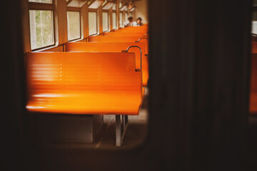 A photo of the interior of an empty retro train  with orange seats on a bright day, taken through the glass of the door. Commuter train travel.