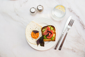 two plates of sandwiches with avocado, tomatoes, fried eggs, two glasses of water with lemon on light background.