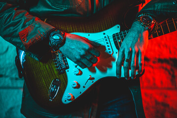 Man holding a guitar at night with jewelry, a watch, color lighting
