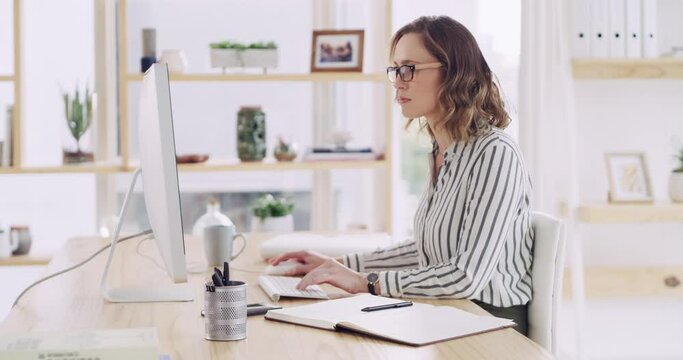 Businesswoman typing out financial reports while working on a computer in her office. Female accountant managing finances and doing bookkeeping using software to compile data and writing notes