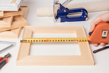 The artist's hand measures the width of the wooden stretcher with a tape measure before trimming and then stretching the canvas