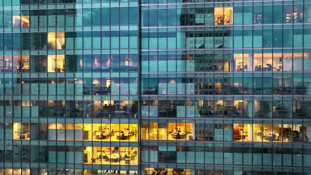 modern glass skyscraper in the evening, end of the working day at a business centre with employees at the illuminated offices, urban lifestyle