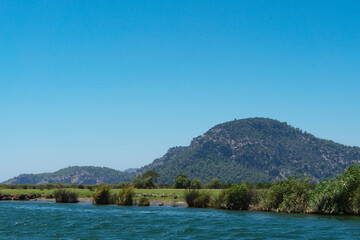 Naklejka premium Rocks, bushes and trees on banks of the Dalyan River, Turkey on a sunny clear summer day. Concept of water travel and the Mediterranean climate. River or water landscape